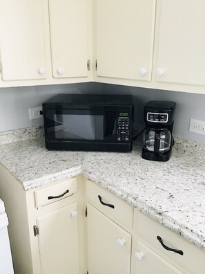 A kitchen with a microwave and coffee maker on a granite countertop, light-colored cabinets, and a white sink.