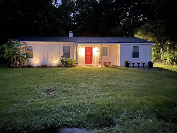 A single-story house with a red door, a small porch, and a well-maintained lawn.