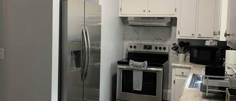 Een moderne keuken met roestvrijstalen apparatuur, witte kasten en een marmeren achterwand.