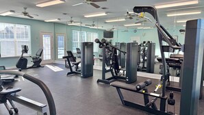 Una palestra con diverse attrezzature per esercizi, ventilatori a soffitto e ampie finestre.