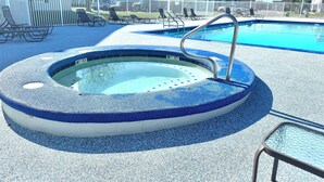 Una vasca idromassaggio con bordo piastrellato in blu e bianco, circondata da un recinto bianco, con una piscina sullo sfondo.