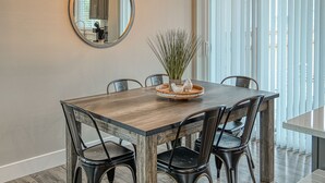 Un comedor con una mesa de madera, sillas negras, un espejo redondo y una lámpara colgante.