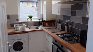 A compact kitchen with a washing machine, a sink, a toaster, and a stove. - Inviting 3-bed Apartment in Southend-on-sea (Southend-on-Sea)