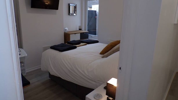 A bedroom with a bed, a bedside table, a nightstand, a TV mounted on the wall, and a window. - Inviting 3-bed Apartment in Southend-on-sea (Southend-on-Sea)