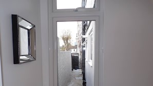 A narrow hallway with a door leading to an outdoor area. A mirror is mounted on the wall to the left. - Inviting 3-bed Apartment in Southend-on-sea (Southend-on-Sea)