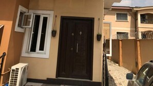 Un edificio residenziale a due piani con facciata beige, una porta d'ingresso marrone scuro e un piccolo condizionatore d'aria al piano terra.