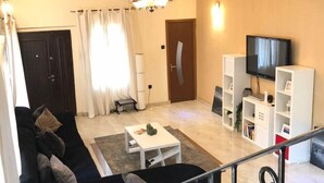 Un soggiorno con un divano nero, un tavolino da caffè bianco e una TV su un mobile.