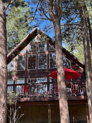 Une cabane avec une façade en bois, de grandes fenêtres et un balcon agrémenté de parasols rouges.