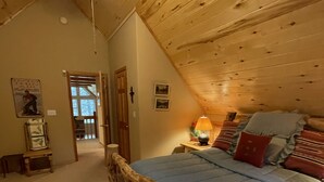 A bedroom with a sloped ceiling, a wooden bed frame, a blue bedspread, and a nightstand with a lamp. - Nestled in the pines on 2 acres, secluded, close-to-nature house. Pet-Friendly! (Angel Fire)