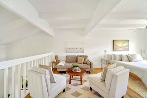 Een ruime woonkamer met een hoge plafond, een witte balustrade, een zithoek, een salontafel en een schilderij aan de muur.