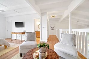 A spacious living area with two grey armchairs, a wooden coffee table with a plant, and a television mounted on the wall. - Puamana 8B · Puamana Repose (Princeville)