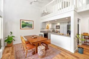 Een moderne keuken met witte kasten, een eethoek met een houten tafel en stoelen, en uitzicht op de woonkamer.