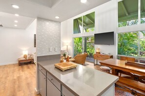 Eine moderne Küche mit einer großen Kochinsel, einem Essbereich mit Holztisch und -stühlen sowie einem an der Wand befestigten Fernseher.