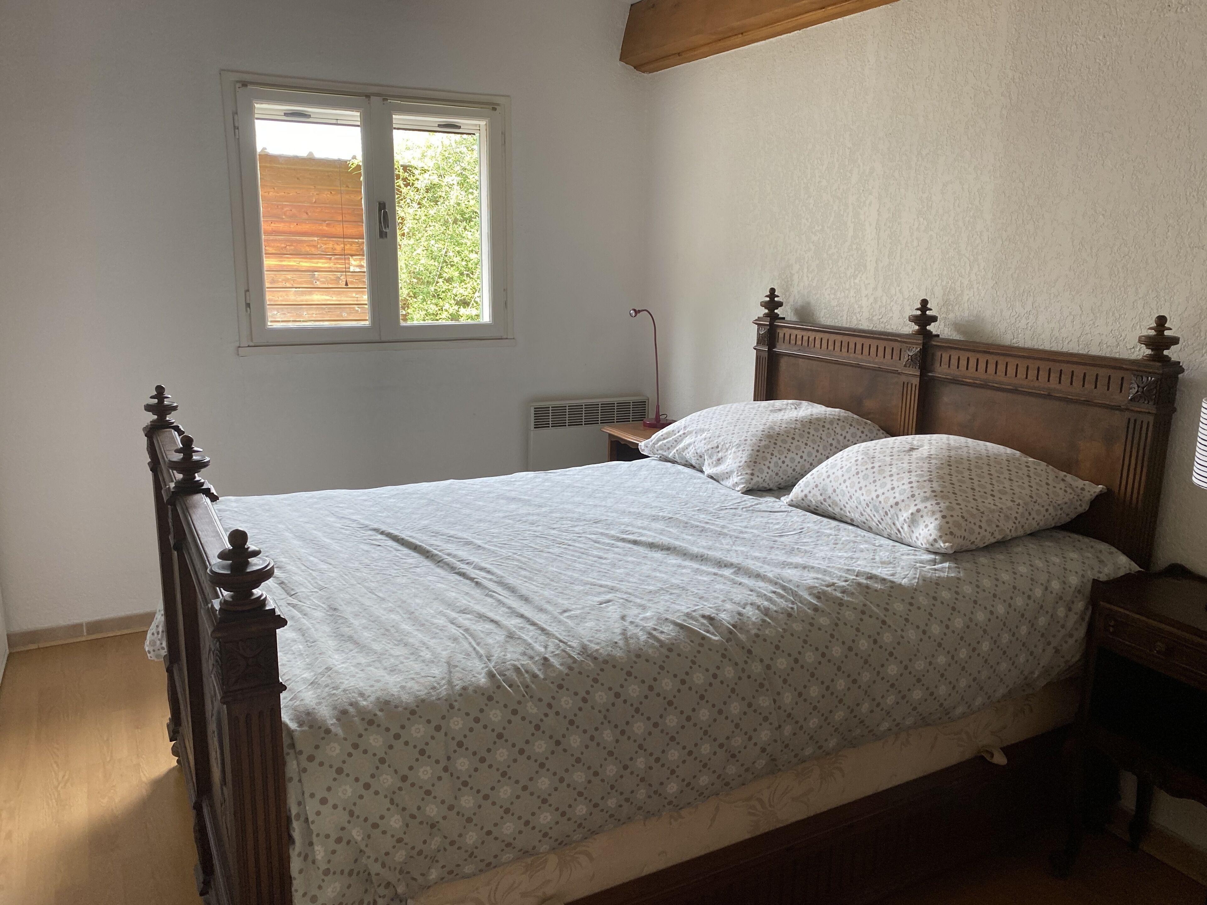 Un letto singolo con testiera in legno, un comodino, una finestra con vista sul verde e un termosifone.
