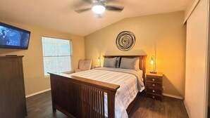 A bedroom with a bed, a ceiling fan, a TV, a window with blinds, a bedside table with a lamp, and a wall art piece. - Relaxing Foothills Home RV Hookup and Parking (Yuma)