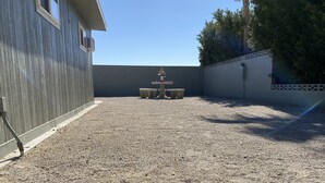 A gravel courtyard with a concrete table and chairs, surrounded by walls and a wooden building. - Relaxing Foothills Home RV Hookup and Parking (Yuma)