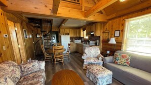 Un acogedor interior de cabaña con una zona de comedor de madera, un sofá y una pequeña cocina.