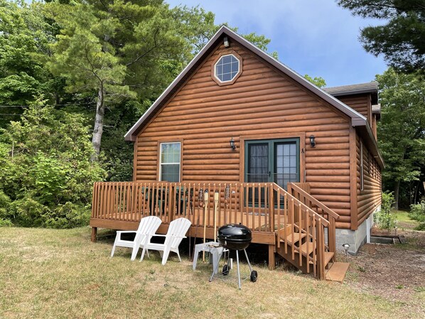 A log cabin with a deck, two white chairs, and a grill.