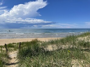 Een strand met zand, gras en een boot op het water.