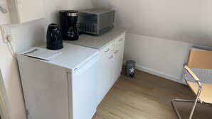 A compact kitchenette with a white refrigerator, a coffee maker, a microwave, and a trash bin. - Old Town Apartment Hameln App 1 (Hameln)