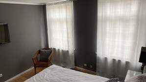 A bedroom with a bed, a chair, and two windows with curtains. - Old Town Apartment Hameln App 1 (Hameln)