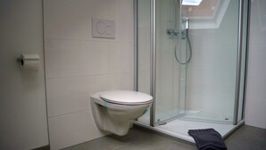A modern bathroom with a toilet, a glass shower enclosure, and a towel on the floor. - Old Town Apartment Hameln App 1 (Hameln)