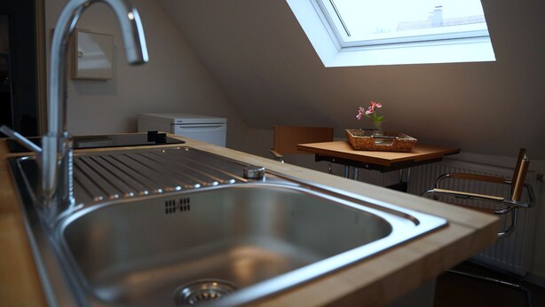 A kitchen with a modern stainless steel sink, a small table with a basket and flowers, and a skylight above. - Old Town Apartment Hameln App 1 (Hameln)