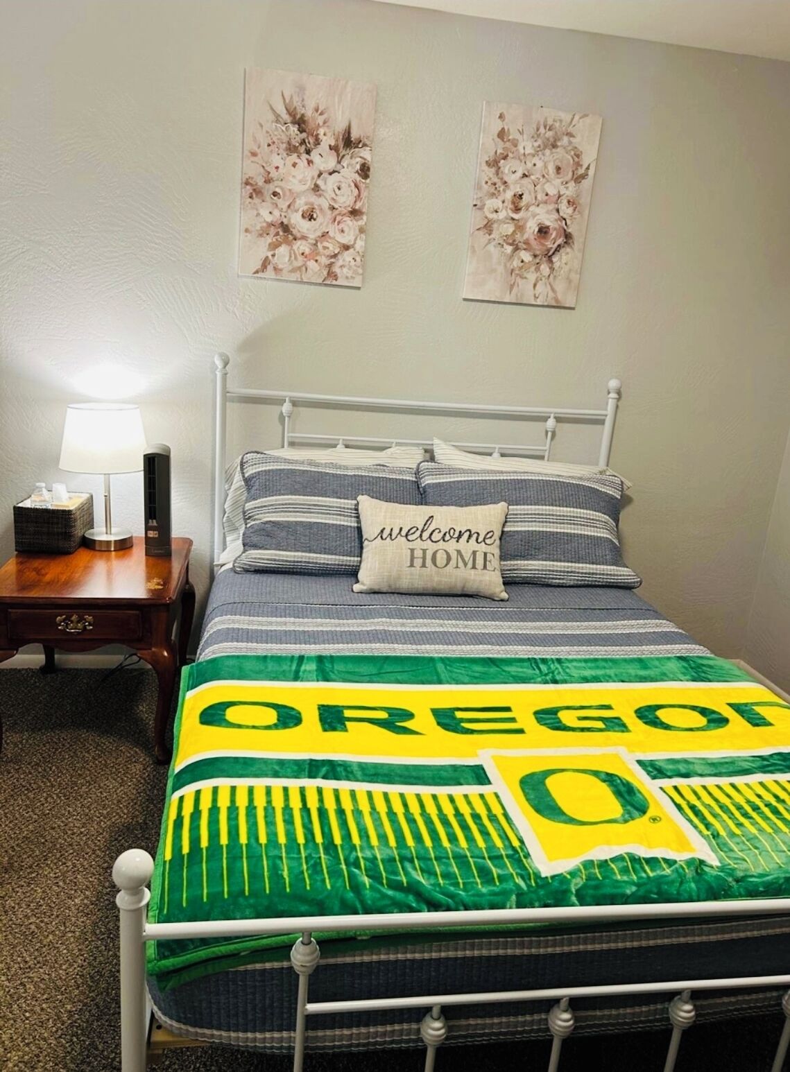 A bedroom with a bed, a bedside table, a lamp, and two wall art pieces.