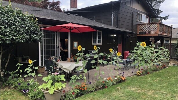 Eine Terrasse mit Sitzgelegenheiten im Freien, einem roten Sonnenschirm und Sonnenblumen.