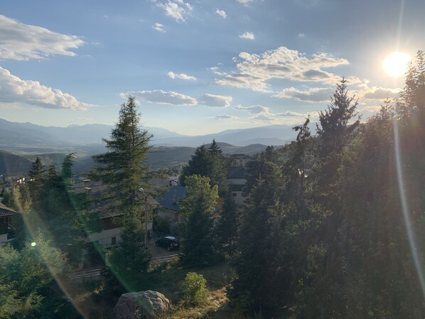 A mountainous landscape with a clear sky, trees, and buildings in the valley.