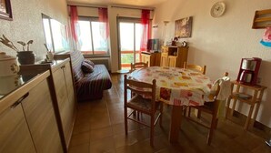 A cozy kitchen with a dining table, chairs, and a sofa. There is a window with curtains, a clock on the wall, and a small cabinet with a microwave. - Apartment in residence with superb view and parking (Font-Romeu-Odeillo-Via)