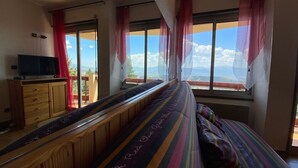 A room with a large window, a bed with striped bedding, a wooden bench, and a television on a wooden cabinet. - Apartment in residence with superb view and parking (Font-Romeu-Odeillo-Via)