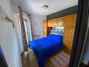 A bedroom with a bed, wooden cabinets, a window with curtains, and a door. - Apartment in a residential complex with a spectacular view and parking space (Font-Romeu-Odeillo-Via)