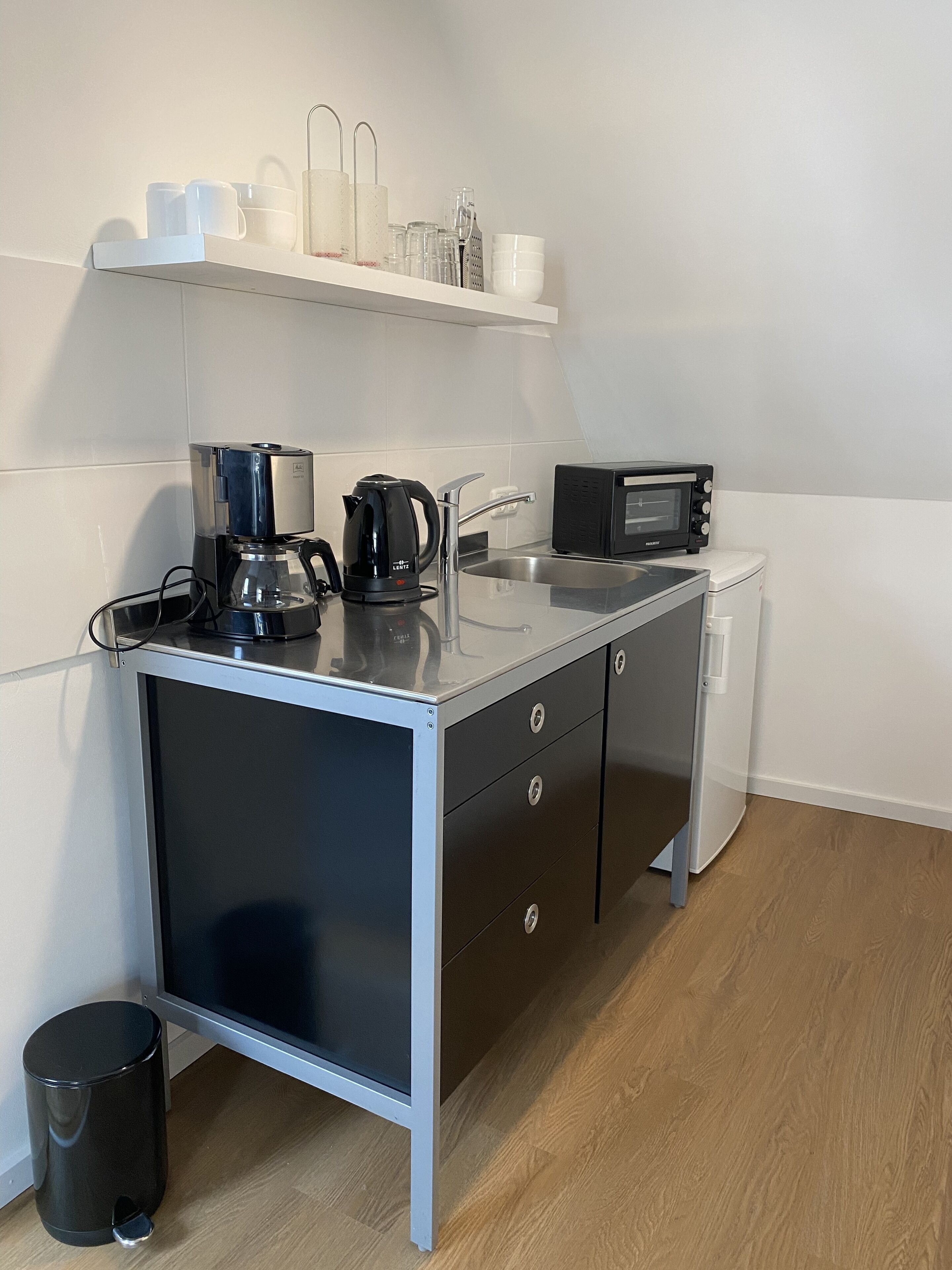 Eine moderne Küchenzeile mit Kaffeemaschine, Mikrowelle und kleinem Kühlschrank.