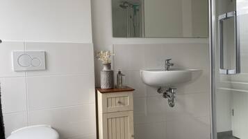 A bathroom with a toilet, a sink, a mirror, and a shower.