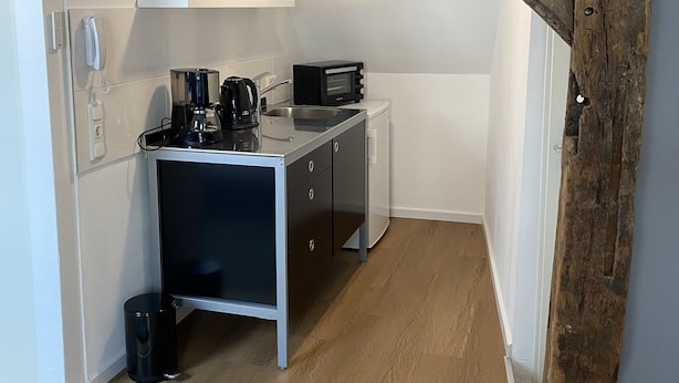 Une cuisine compacte avec un plafond orné de poutres en bois, une machine à café, un four à micro-ondes et un petit plan de travail.