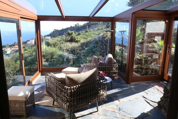 Um quarto iluminado pelo sol com vista para uma encosta, mobiliário de vime e piso de pedra.