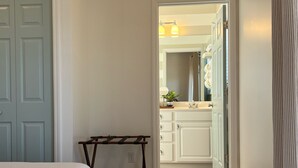 Une chambre à coucher comprenant un lit, une petite table et une porte donnant sur une salle de bain équipée d’un lavabo et d’un miroir.