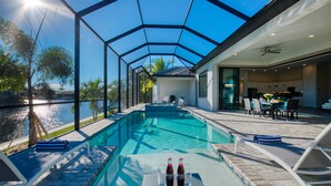Une piscine entourée de parois en verre, des chaises longues et une table avec des boissons.
