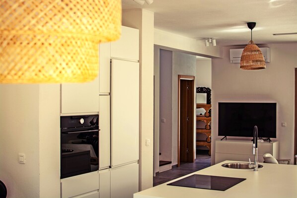 A modern kitchen with built-in appliances, a central island with a sink, and a television in the background.