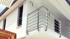 Una casa moderna de dos pisos con un balcón, un conjunto de sofás y una mesa de vidrio.