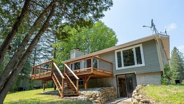 A two-story house with a wooden deck and a stone retaining wall. - Magical Moments Hot tub & Swimmable Lake (Amherst)