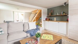 A modern living room with a sofa, coffee table, and a staircase leading to a kitchen area. - Magical Moments Hot tub & Swimmable Lake (Amherst)