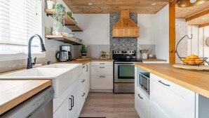 A modern kitchen with white cabinets, a wooden countertop, a built-in oven, and a backsplash with a geometric pattern. - Magical Moments Hot tub & Swimmable Lake (Amherst)