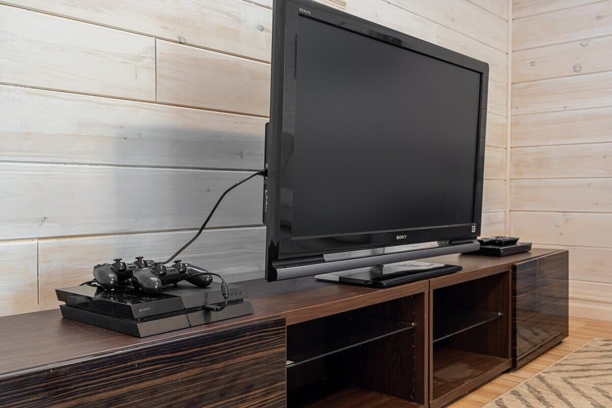 A modern living room with a large flat-screen TV on a wooden stand, a gaming console, and a small cabinet.
