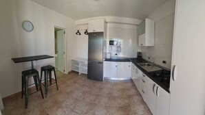 A compact kitchen with a refrigerator, stove, sink, and a small dining area with stools. - Modern Studio in Rural Tinajo with Patio, BBQ & Coastal Views – Perfect Getaway! (La Costa)