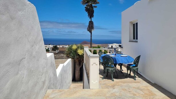 A terrace with a table and chairs, overlooking a coastal landscape. - Modern Studio in Rural Tinajo with Patio, BBQ & Coastal Views – Perfect Getaway! (La Costa)