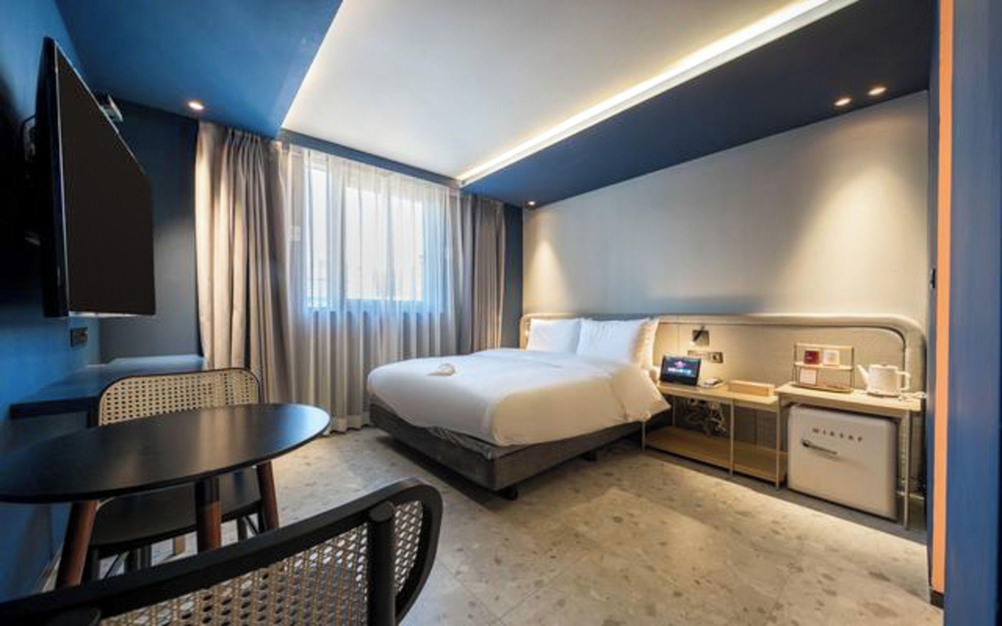 A hotel room with a bed, bedside table, TV, and a desk with a chair.
