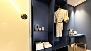Een moderne badkamer met een donkerblauwe wand, een witte badjas hangend aan een rek, netjes opgevouwen handdoeken op planken en een houten stoel.