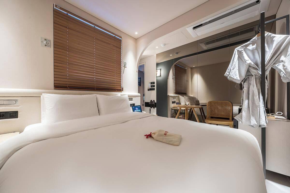 Habitación de hotel con una cama grande, una mesita de noche, un armario y un baño visible a través de un arco.